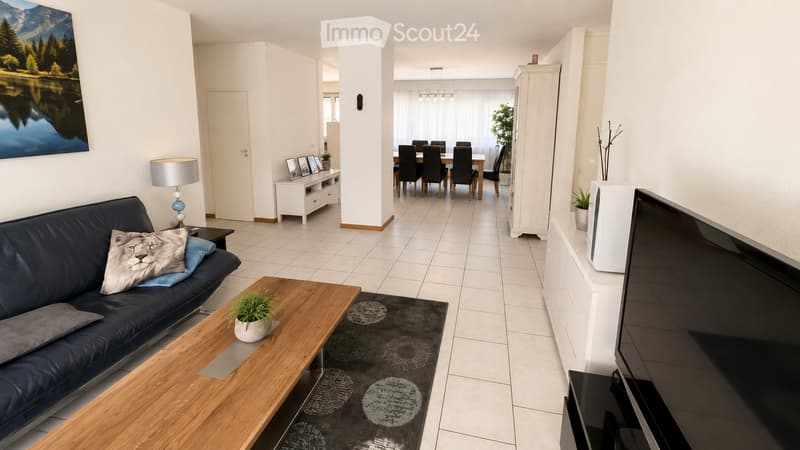 Open-plan living and dining area with a dark blue sofa, wooden coffee table, dining table with chairs, and a TV screen on a white cabinet.