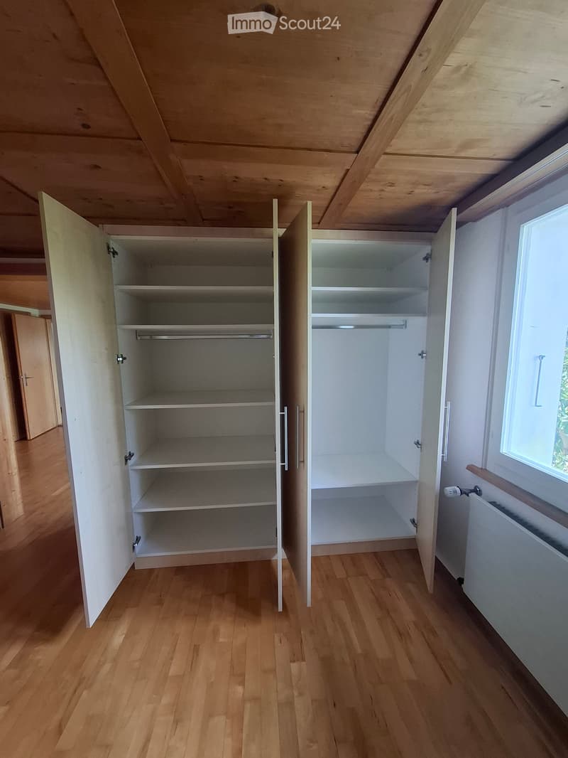 Empty room with wooden flooring, white walls, and built-in wardrobes with open doors and shelves.
