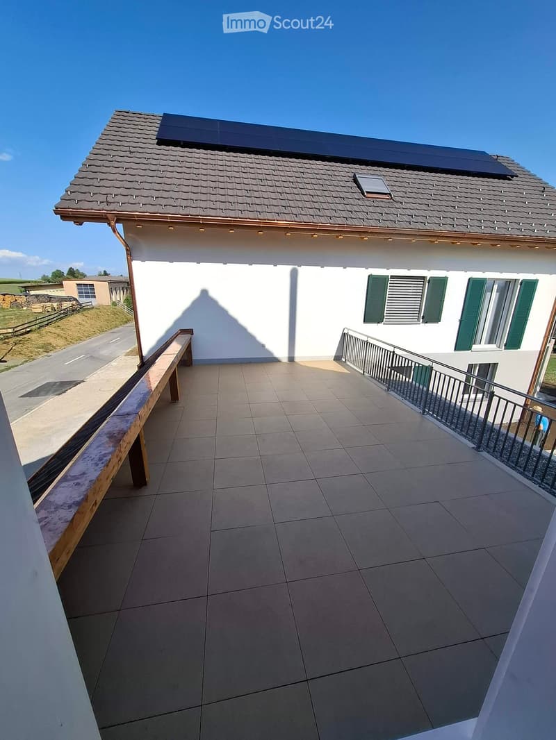 Balcony with tiled floor, wooden bench, metal railing, and view of the house and surrounding area.