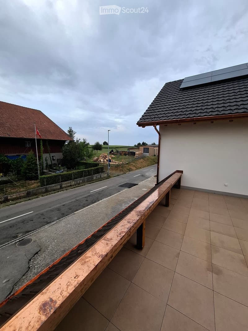Balcony with tiled floor, wooden railing, overlooking a road and neighboring houses.