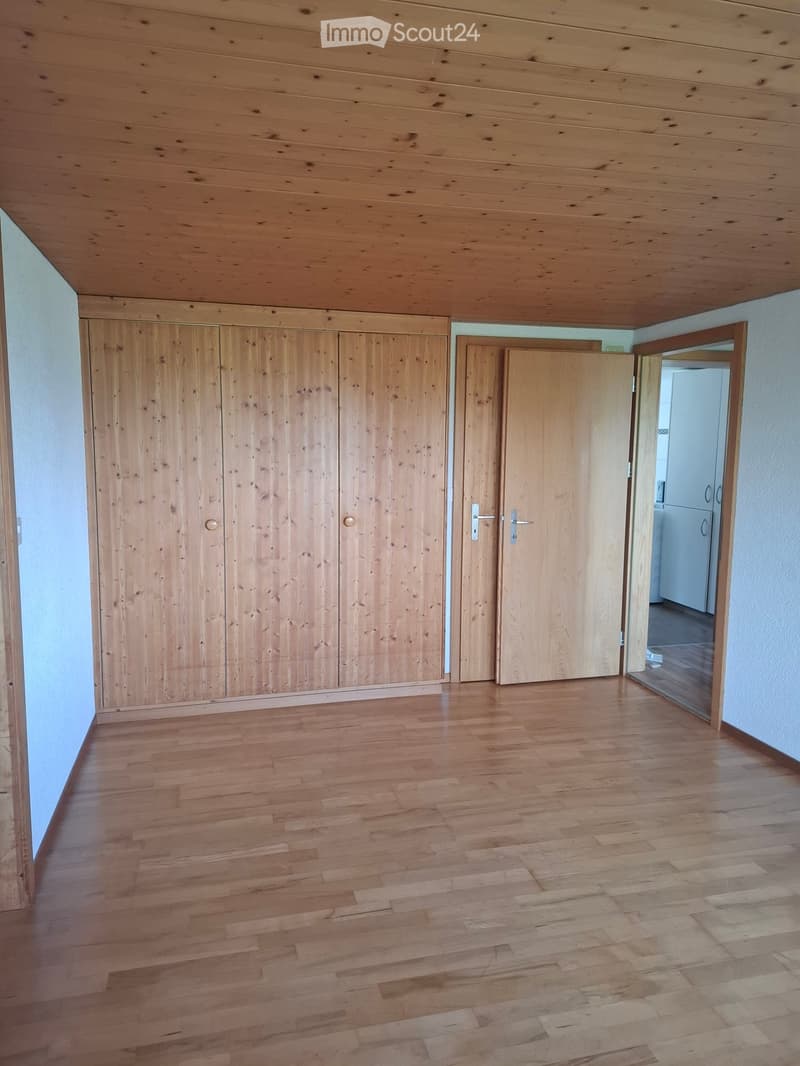 Empty room with wooden floor, wooden closet, and open doorway leading to another room.