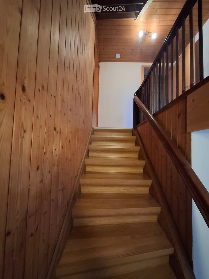 Wooden staircase with a handrail, wooden walls, and ceiling lights.