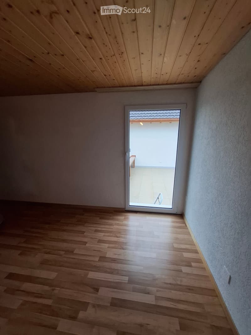 Empty room with wooden flooring and white walls, featuring a sliding glass door leading to a balcony or outdoor area.
