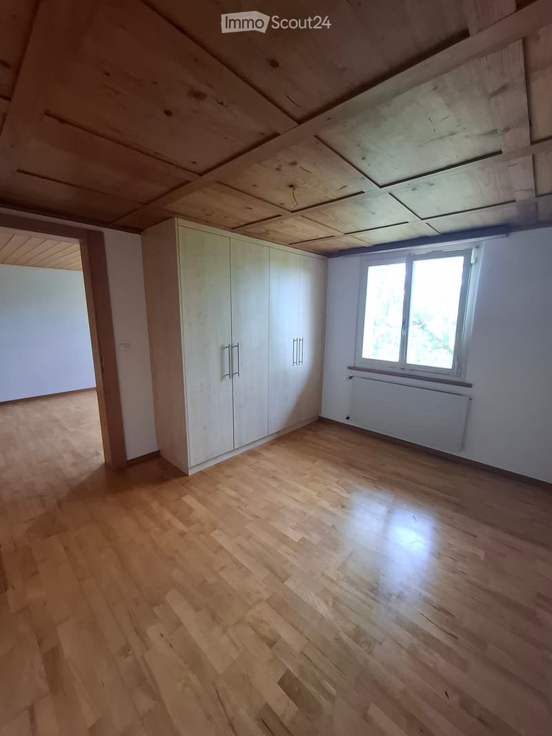 Empty attic room with wooden flooring, white walls, built-in wardrobes, and a large window letting in natural light.