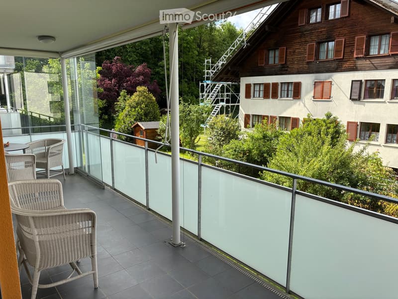 Balcony with tiled floor, glass railing, and outdoor furniture including chairs and a small table.