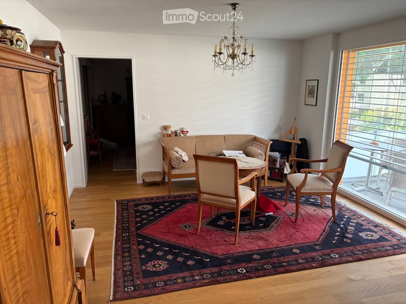 A well-furnished living room with a wooden floor, a large patterned rug, a sofa, chairs, a round table, and a chandelier.