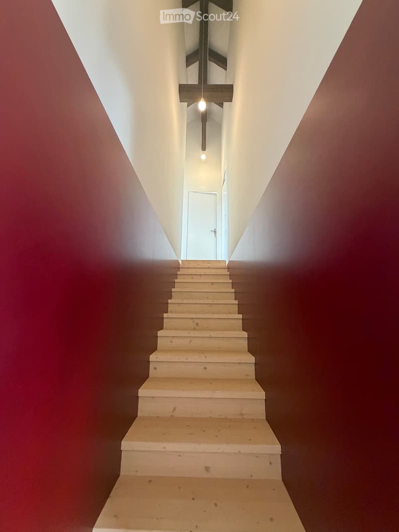 Modern staircase with light-colored steps and dark walls, featuring a single pendant light fixture hanging from the ceiling.