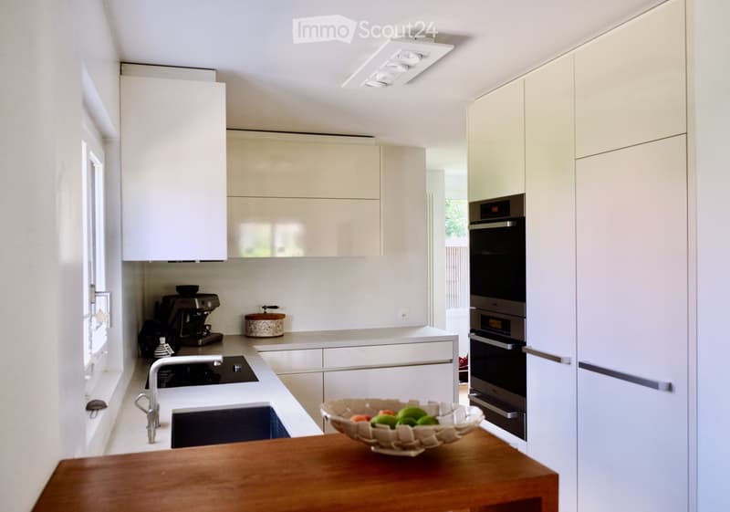 Modern kitchen with white cabinets, stainless steel appliances, and a wooden table with a bowl of fruit.