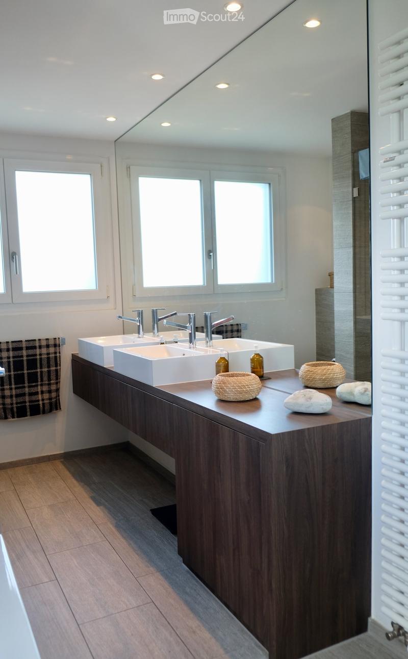 Modern bathroom with a double sink vanity, sleek wooden cabinetry, and decorative items including wicker baskets and stones on the countertop.
