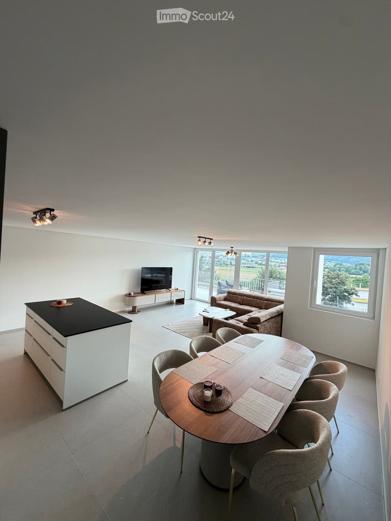 Open-plan living and dining area with a sofa, coffee table, dining table with chairs, and a kitchen island.