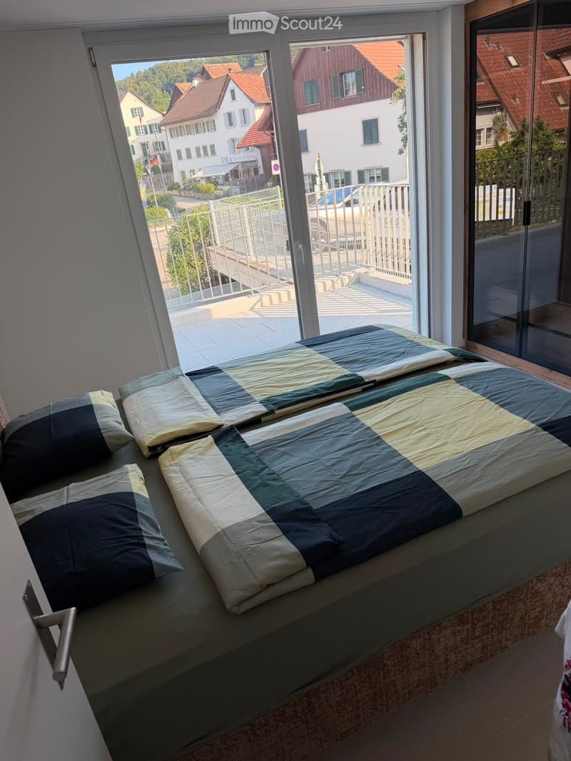 Bedroom with a large window and a bed with a blue and white checkered duvet and matching pillows.