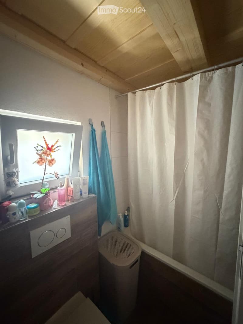 Cozy bathroom with a window, sink, mirror, shower curtain, towels, and a small stool. The window has a decorative flower on the sill.