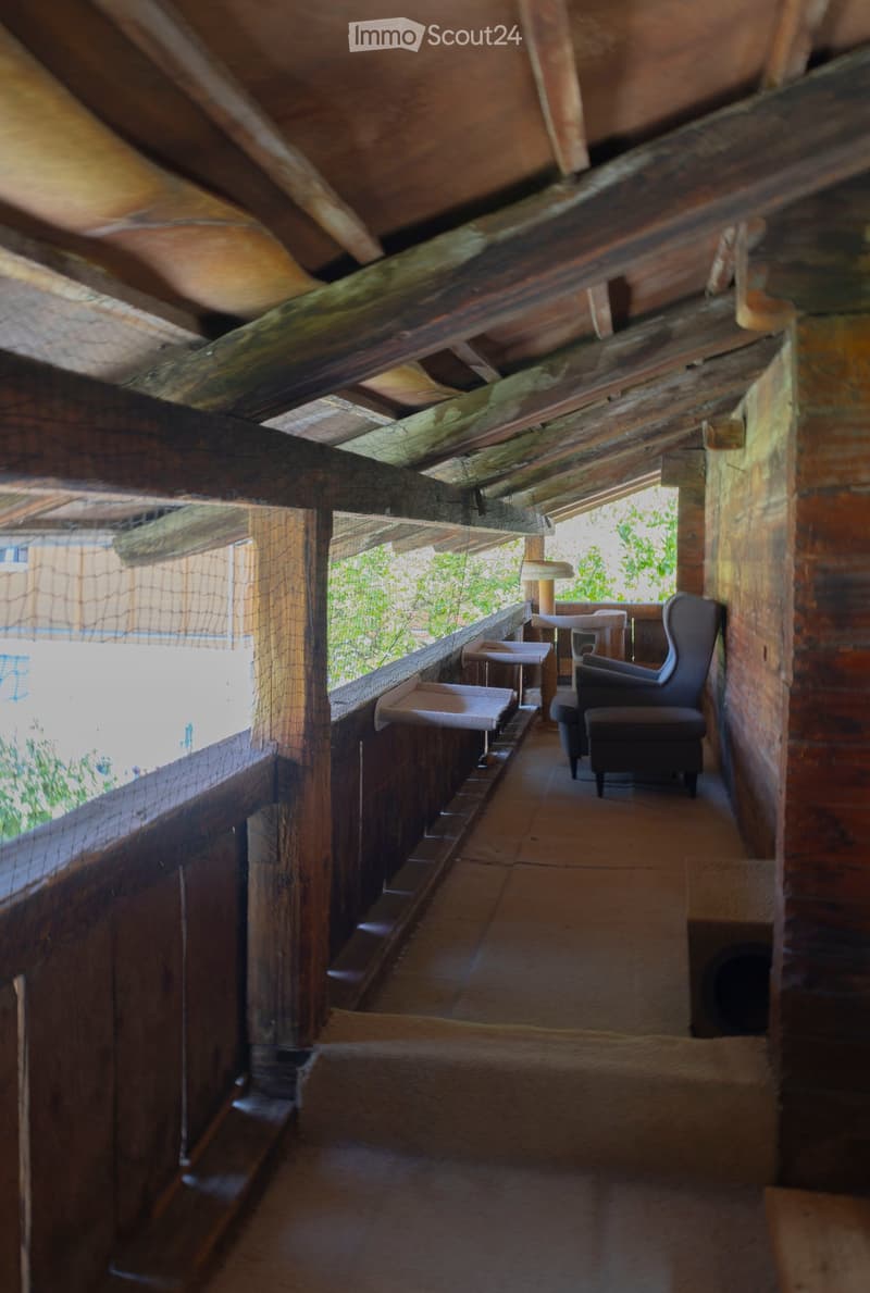 Balcony with wooden beams, brick walls, and outdoor furniture including chairs and a table.