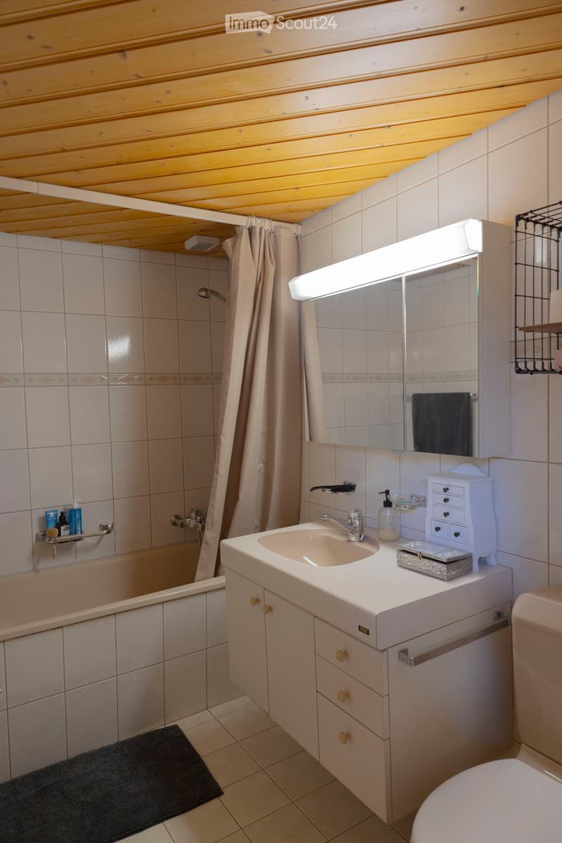 Bathroom with a sink, mirror, toilet, bathtub, and shower area. Features a wooden ceiling, tiled walls, and a small cabinet with drawers.