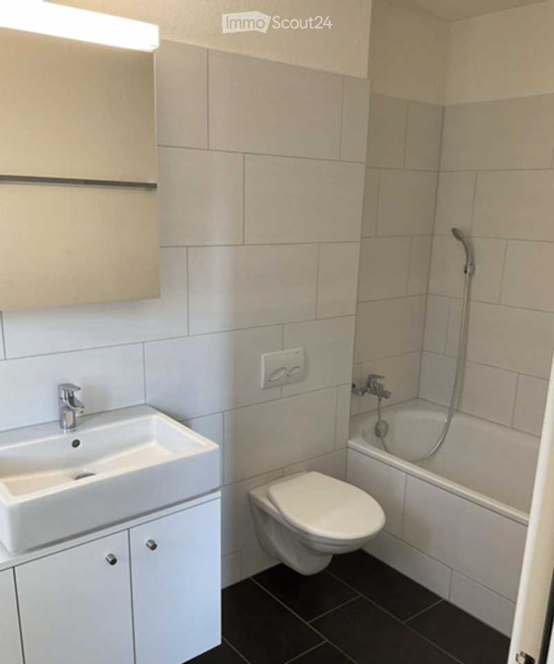 Modern bathroom with white tiles, a sink, toilet, bathtub, and a mirror above the sink.