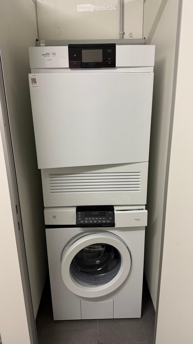 A compact bathroom with a stacked washing machine and dryer unit, featuring modern control panels and sleek white finishes.