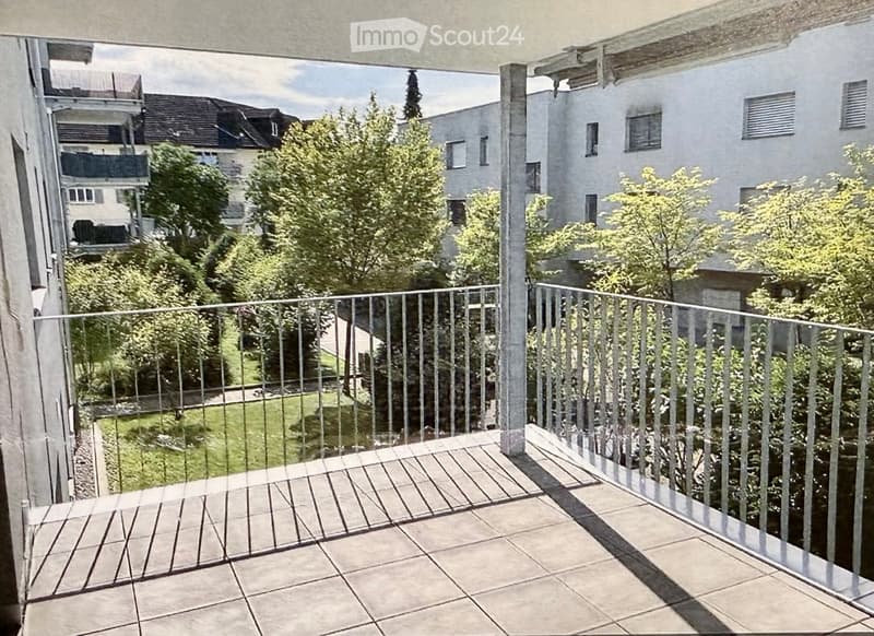 Balcony with wooden decking, metal railing, and view of greenery and buildings.
