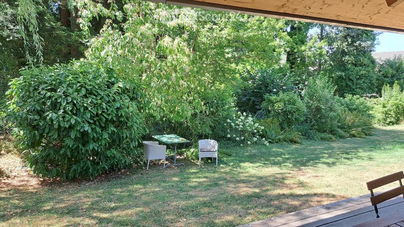 Garden area with a small table and two chairs, surrounded by lush greenery and trees.