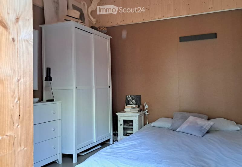 A modern bedroom with a bed, nightstand, wardrobe, and decorative items including a lamp and books.