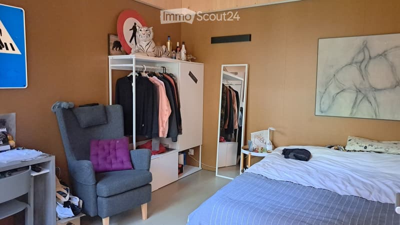 Cozy bedroom with a bed, grey armchair, wardrobe, mirror, and artwork on the wall.