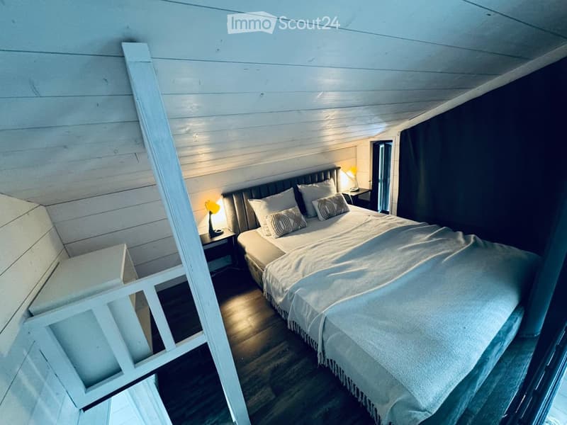 Cozy bedroom with a double bed, nightstand, and lamp, featuring wooden walls and a slanted ceiling.