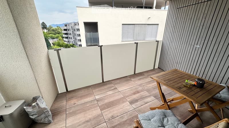 Balcony with wooden table and chairs, tiled floor, white privacy screen, and city view.