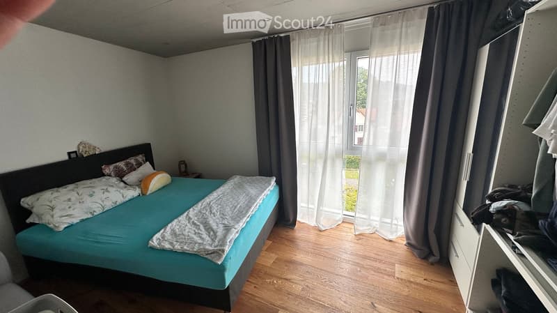 Bedroom with a blue bed, pillows, a wardrobe, and a window with curtains.
