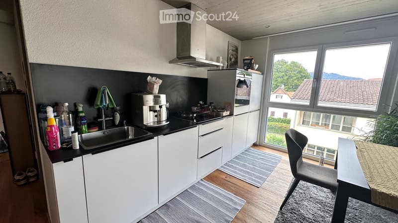 Modern kitchen with white cabinets, black countertops, stainless steel appliances, and a large window overlooking a residential area.