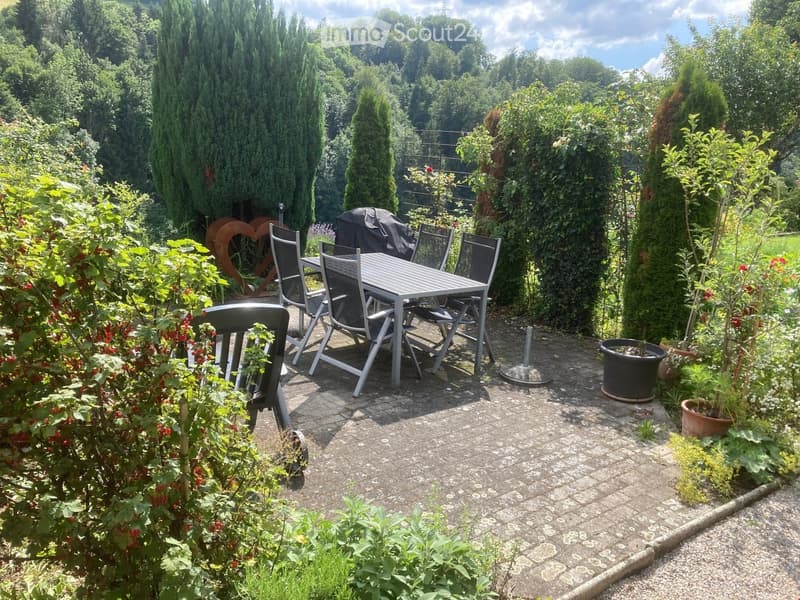 Garden patio with a table, chairs, umbrella, and surrounding greenery.
