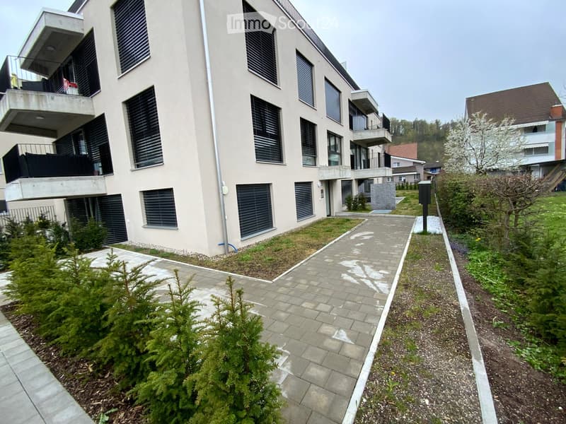Modern multi-story residential building with balconies, large windows, and surrounding greenery.
