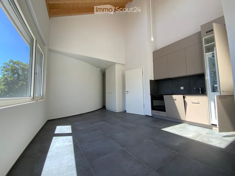 Modern kitchen with light-colored cabinets, dark tiled floor, and large windows allowing natural light to fill the space.