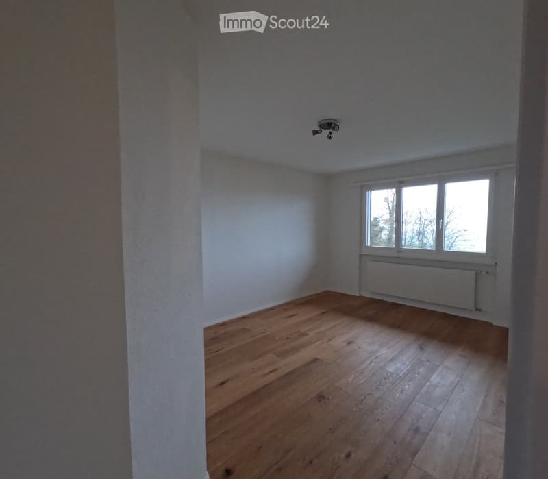 Empty room with wooden flooring, white walls, and a window with a radiator below it.