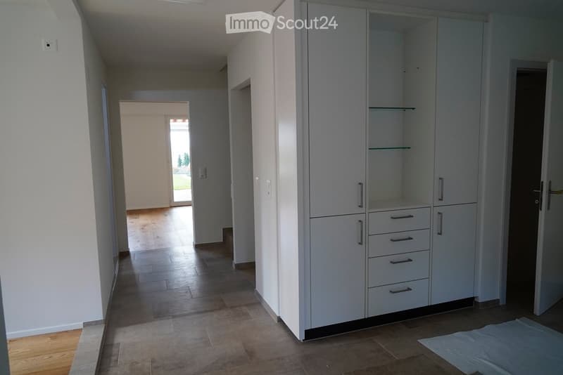 Empty hallway with light-colored walls, wooden flooring, and built-in white storage units with glass shelves and drawers.