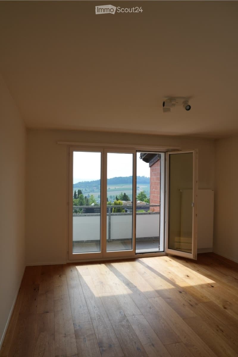 Empty room with wooden flooring, large sliding glass doors leading to a balcony, and natural light streaming in.