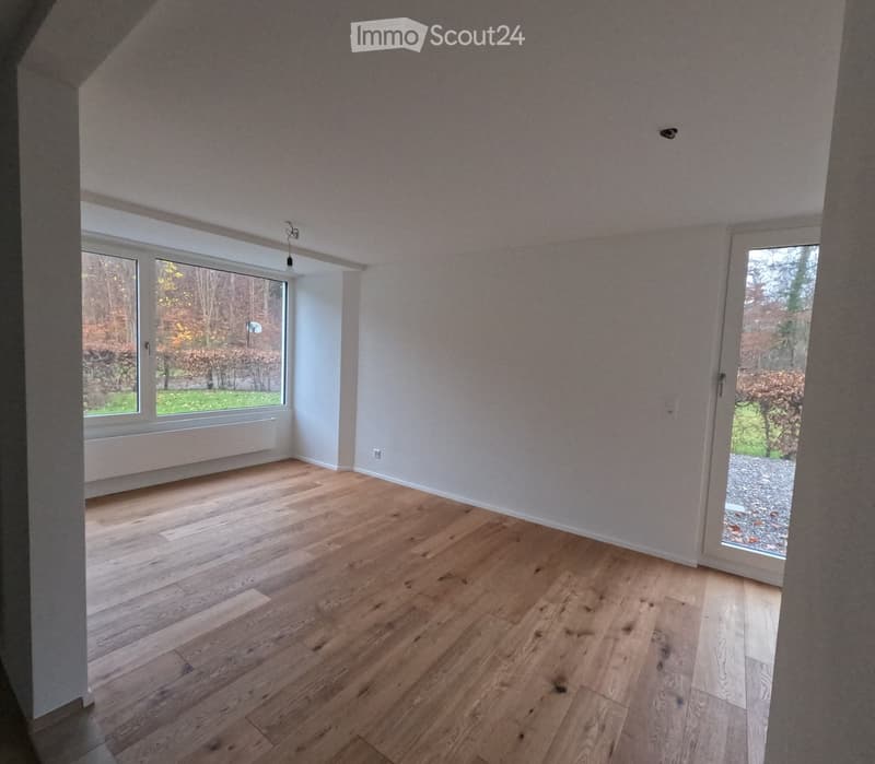 Empty room with wooden flooring, large windows, and a sliding glass door leading to an outdoor area.