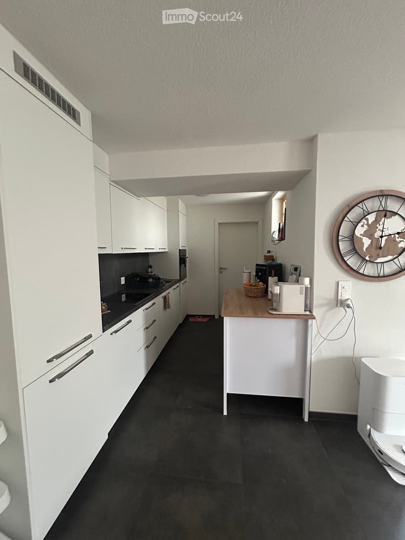 Modern kitchen with white cabinets, dark countertops, and a small island with a microwave and other appliances.