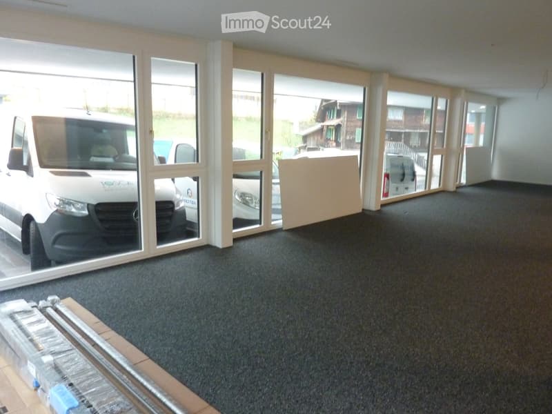 Empty room with large glass doors leading to an outdoor area, carpeted floor, and a few stacked items in the corner.