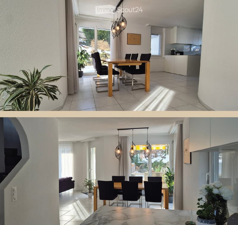 Bright, open-plan dining and kitchen area with a wooden dining table, black chairs, modern kitchen cabinets, and potted plants. A sofa is visible in the adjacent living space.