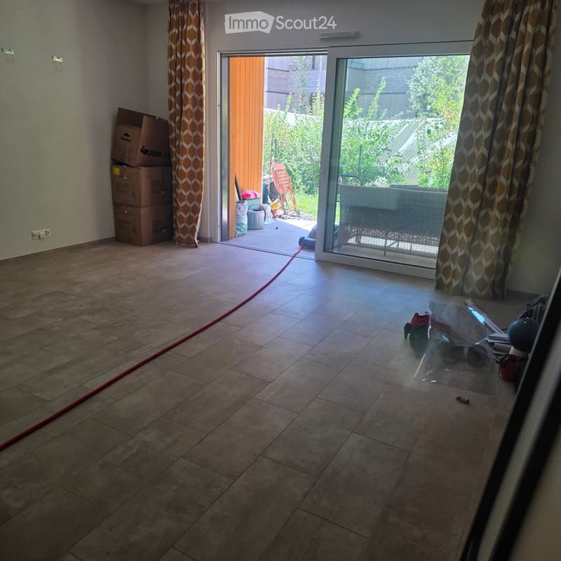 Empty room with tiled floor, large sliding glass door leading to outdoor area, stacked boxes, and a few scattered items near the entrance.