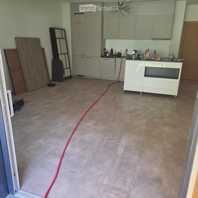 Empty kitchen with light grey cabinets, a white countertop, and a tiled floor. Various items and tools are scattered around, indicating ongoing renovation or cleaning.