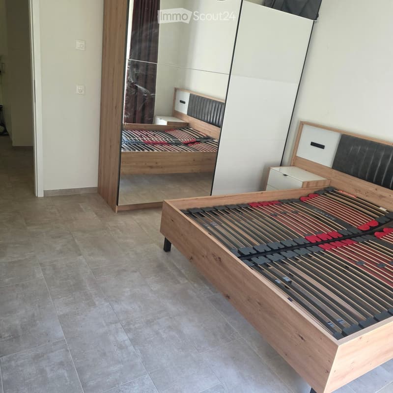 Modern bedroom with a wooden bed frame and a large mirror reflecting the bed and part of the room.