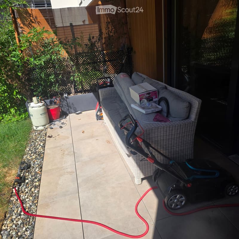 Garden area with a wicker sofa, lawn mower, garden hose, barrel, and bucket.