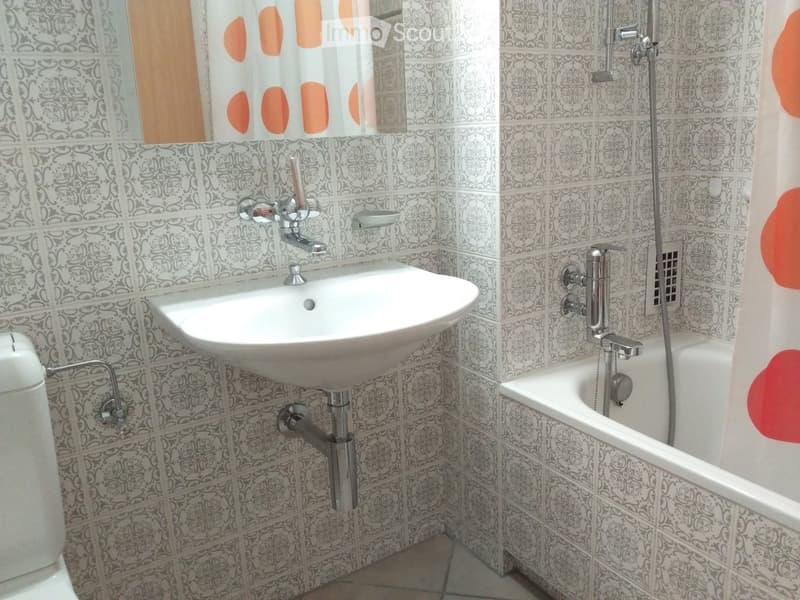 Bathroom with a white sink, bathtub, and toilet, featuring patterned tiles and a shower curtain with orange accents.
