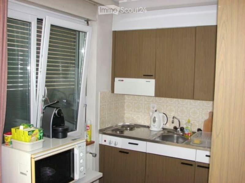 A compact kitchen with wooden cabinets, a microwave, coffee maker, stove, sink, and various small appliances.
