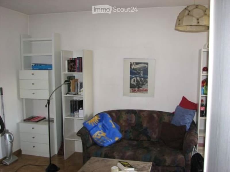A cozy living room with a patterned sofa, colorful cushions, a wooden coffee table, a bookshelf filled with books, and a floor lamp.