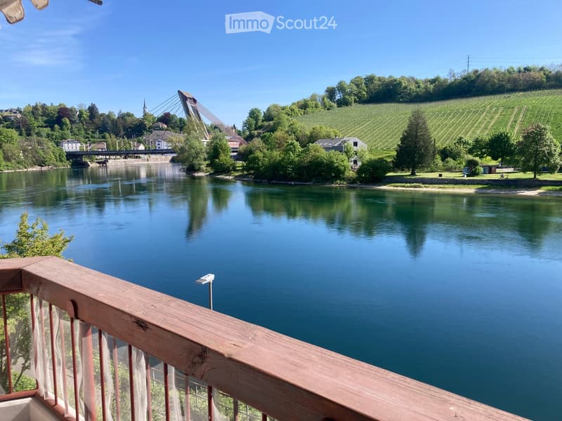 Balcony overlooking a river with a bridge, green hills, and vineyards in the background.