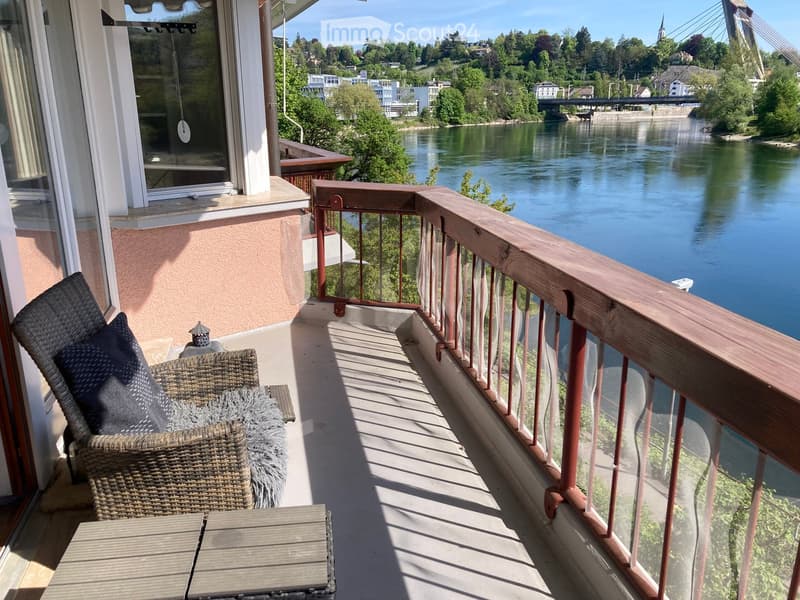 Balcony with wicker chair, small table, and scenic river view.