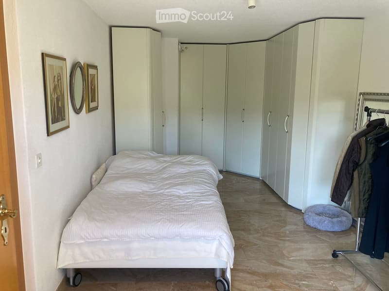 Bedroom with a single bed, large white wardrobe, mirror, picture frames, and a pet bed on the floor.