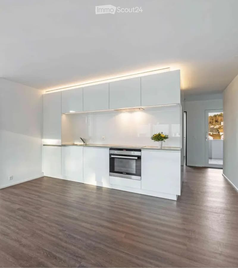 Modern, minimalist kitchen with white cabinets, stainless steel oven, and wooden flooring.
