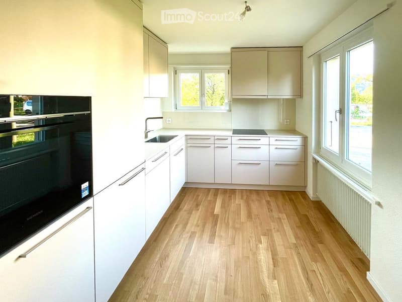 Modern kitchen with light-colored cabinets, wooden flooring, and stainless steel appliances including an oven and sink.